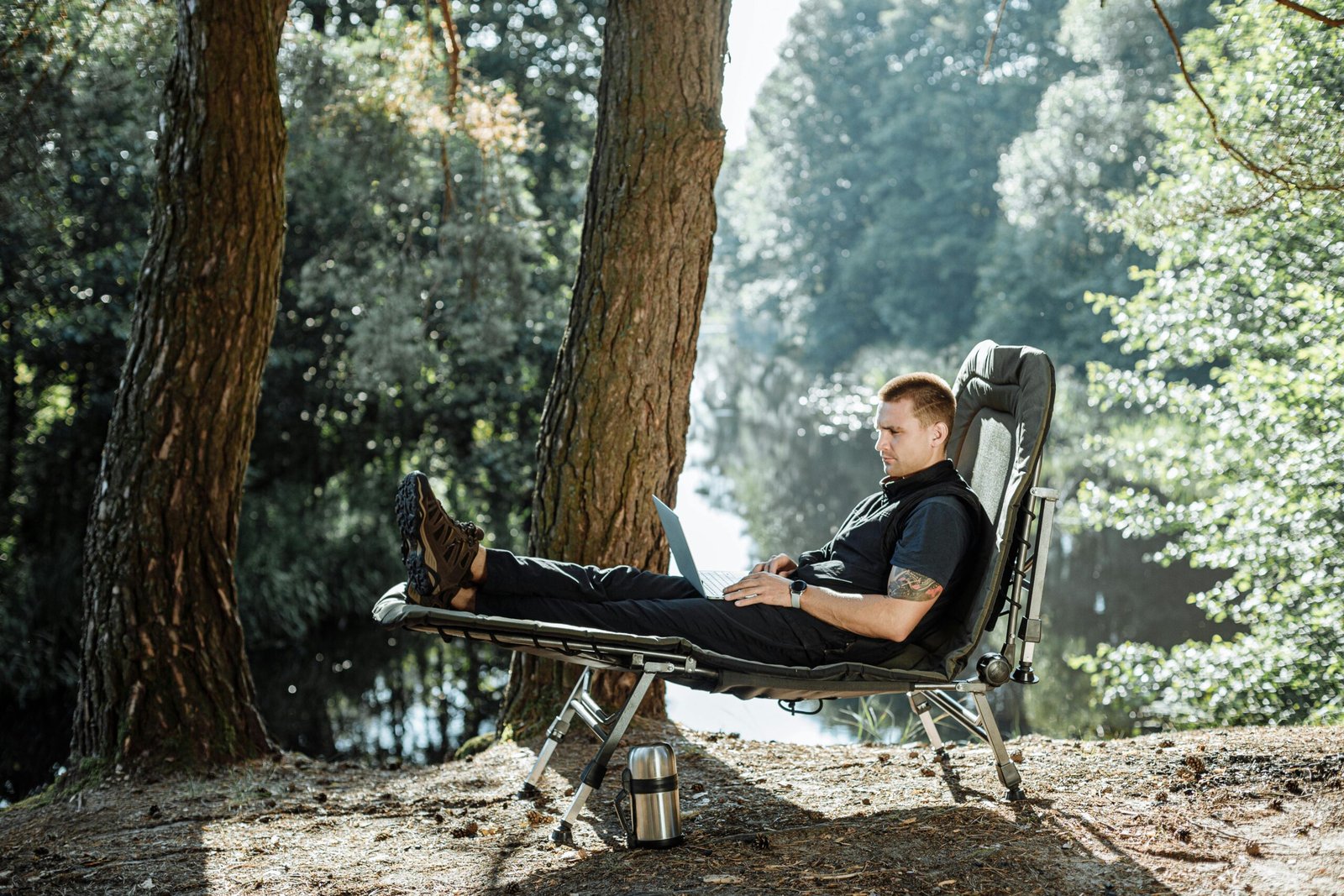 A man enjoys outdoor work on a laptop at a forest campsite.